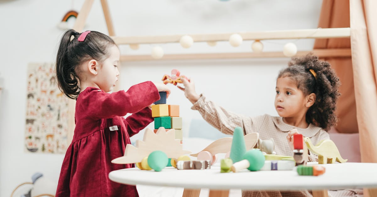 Two young girls enjoying playtime with wooden toys indoors in a warm, colorful playroom.