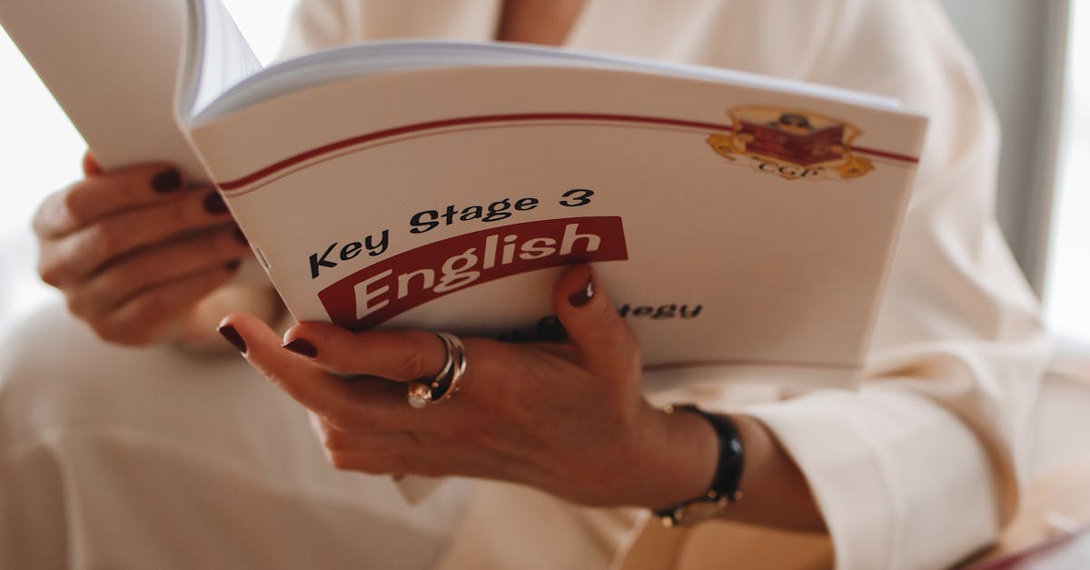 Adult woman reading a Key Stage 3 English book, seated at a wooden table.